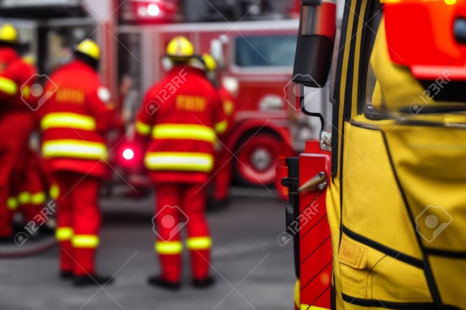 Gruppo di vigili del fuoco in uniforme durante l'operazione antincendio nelle strade della città, vigili del fuoco con il veicolo da combattimento del camion dei pompieri sullo sfondo, emergenza