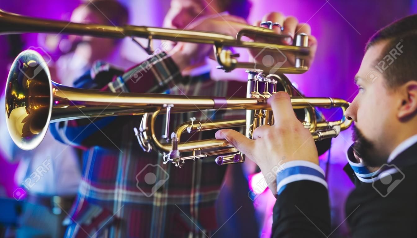 Concert view of a male trumpeter, professional trumpet player with vocalist and musical during jazz band performing in the background