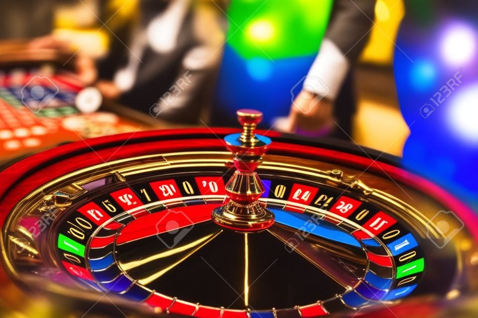 A close-up vibrant image of multicolored casino table with roulette in motion, with casino chips. the hand of croupier, mone and a group of gambling rich wealthy people in the background