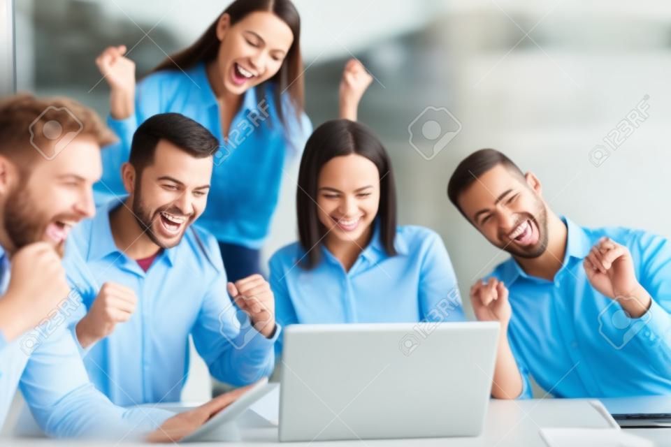 Szczęśliwi ludzie biznesu śmieją się w pobliżu laptopa w biurze. odnoszący sukcesy współpracownicy zespołu żartują i bawią się razem w pracy.