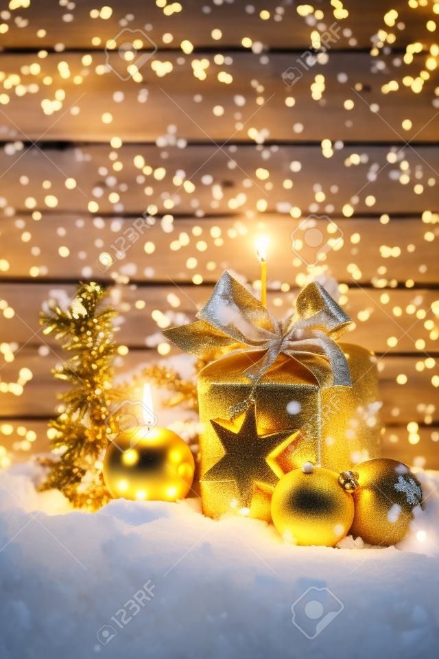 Regalo di Natale dorato, palla di natale, candela sul mucchio di neve contro la parete di legno