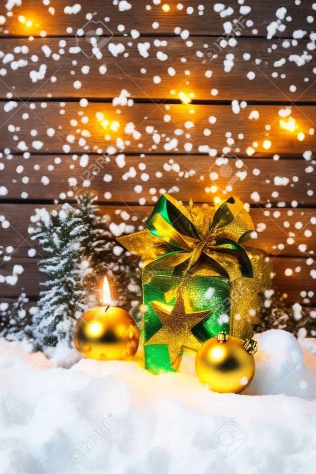 Regalo di Natale dorato, palla di natale, candela sul mucchio di neve contro la parete di legno