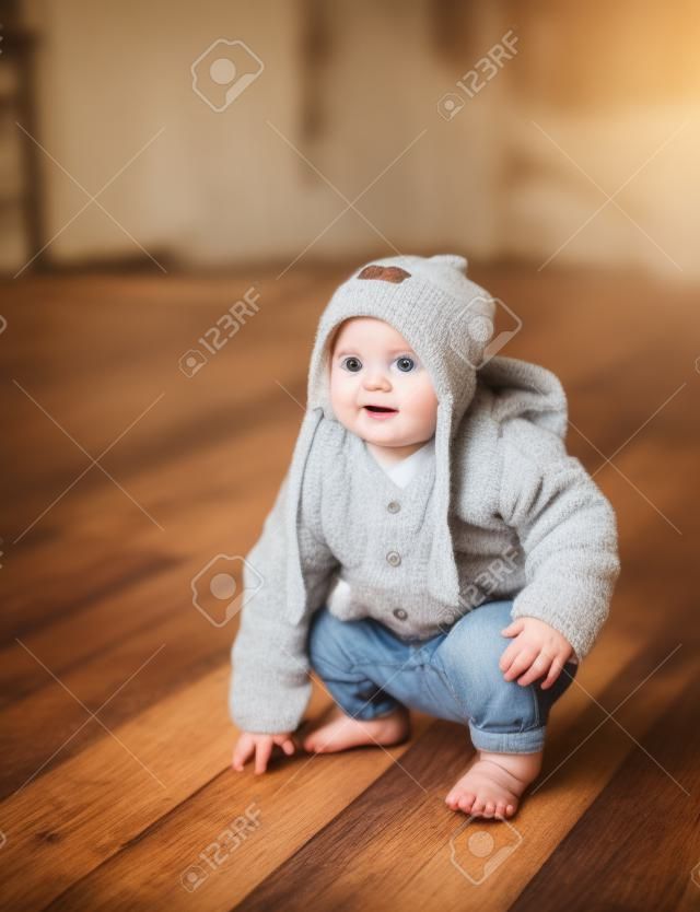 Small adorable infant standing on all fours on wooden floor at home.