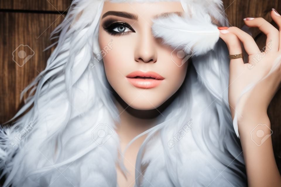 一个相当温柔的年轻时髦的女人，有着长长的卷发，明亮的妆容和白色的蓬松的羽毛，从天使的翅膀，在黑色的布裙上，在木制的背景图片上。