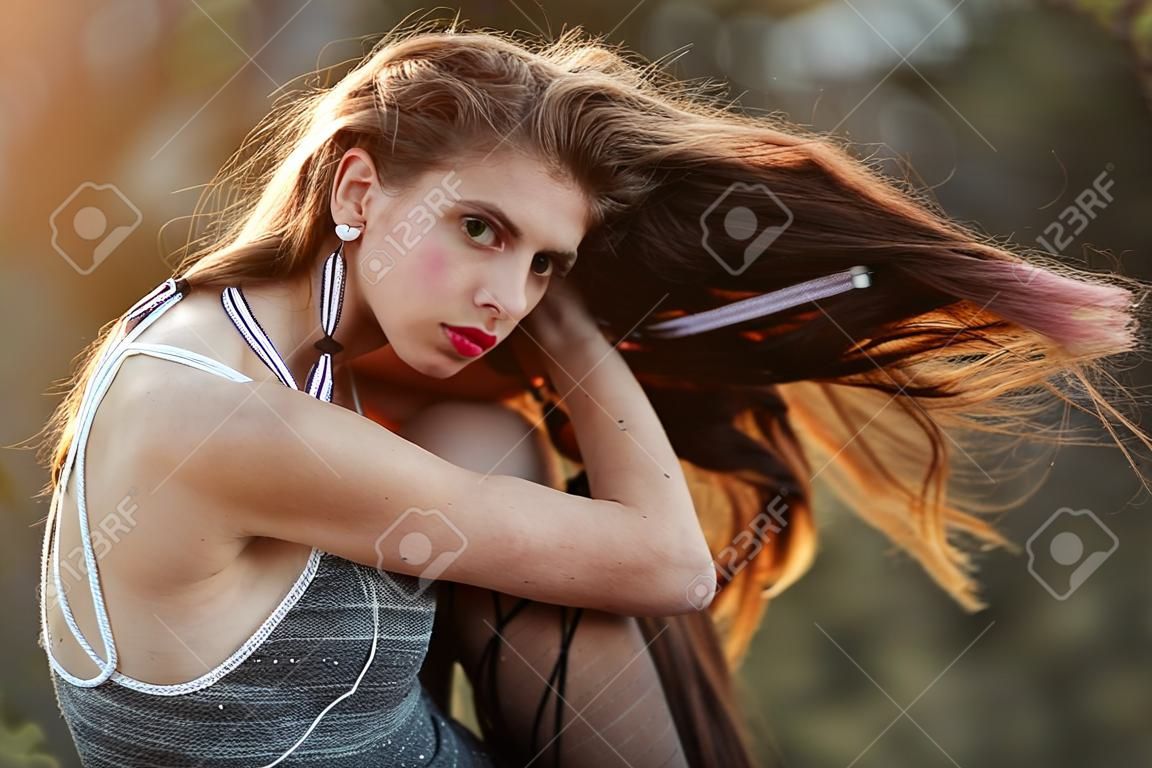 Frau. Mädchen mit langen Indie Frisur, hat weißes Seil im Haar, Make-up, Piercing in Nase im Sommer Kleid bei Sonnenuntergang auf natürlichen Hintergrund, Boho, Stammes-Stil, Garn, Faden Handwerk