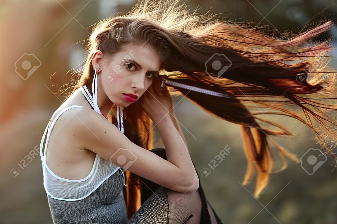 woman. girl with long indie hairstyle, has white rope in hair, makeup, piercing in nose in summer dress at sunset on natural background, boho, tribal style, yarn, thread handicraft