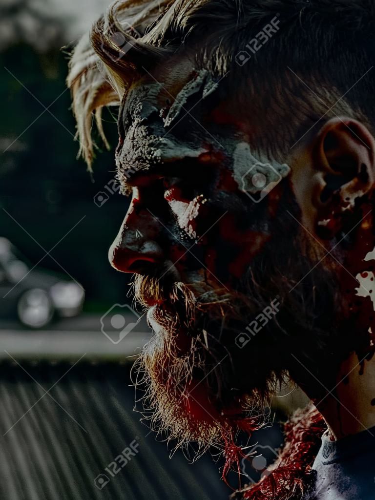 Homme d'Halloween à la barbe sanglante et aux cheveux. Soldat de guerre avec des blessures sur le profil du visage. Concept de fête de vacances. Vampire hipster avec du sang rouge. Zombie sur l'environnement naturel à l'extérieur.