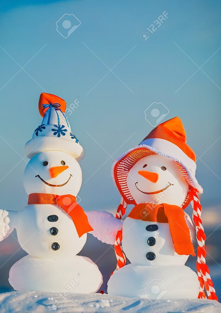Snowmen in hats on natural background. Christmas and new year celebration. Two snow sculptures with smiley faces on blue sky. xmas decorations and ornaments. Winter holidays concept.