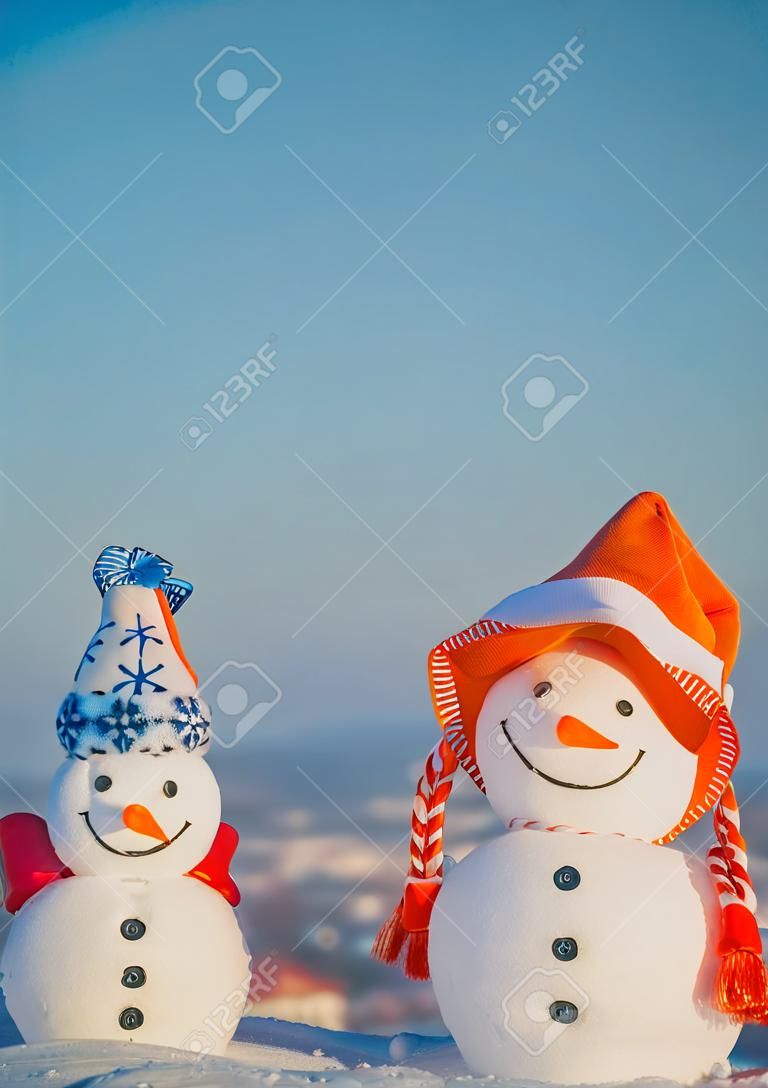 Snowmen in hats on natural background. Christmas and new year celebration. Two snow sculptures with smiley faces on blue sky. xmas decorations and ornaments. Winter holidays concept.