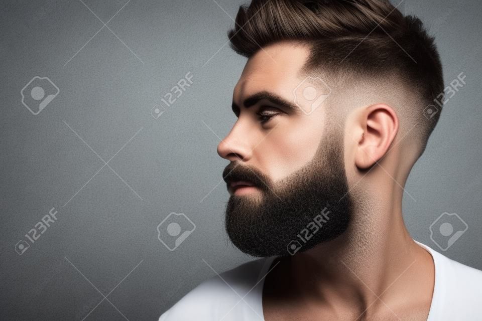 Macho com perfil facial barbudo e elegante pose de cabelo em fundo cinza. Conceito de barbeiro, barbearia, cabeleireiro ou salão de beleza, espaço de cópia
