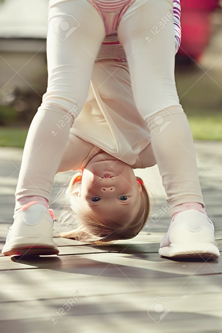 Kid girl stand on head on sunny day outdoor. Sport, yoga, pilates for child. Activity, energy concept. Childhood, playtime, lifestyle.