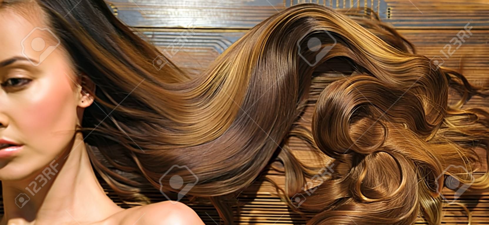 Very long hair on wooden background. Beautiful model with curly hairstyle. Hair Salon concept. Care and hair products.