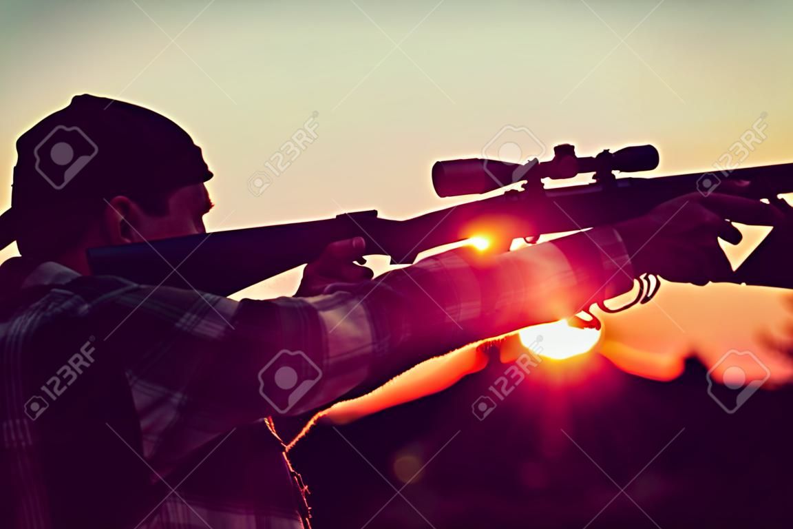 아름 다운 석양에 silhouetted 소총 사냥꾼입니다. 동물을 탐지하는 스코프가 있는 강력한 소총을 든 사냥꾼. 산탄총의 방아쇠를 당겼습니다. 추적.