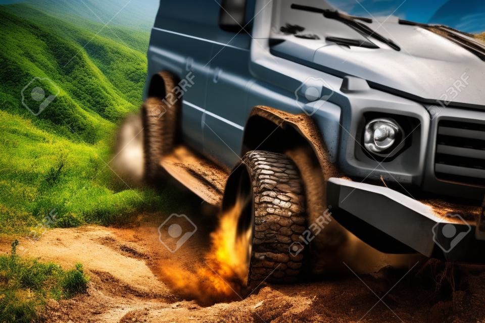 Off-road travel on mountain road. Bottom view to big offroad car wheel on country road and mountains backdrop. Drag racing car burns rubber. Extreme. Off-road car.