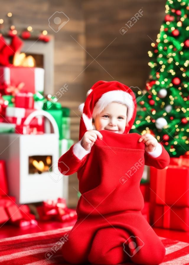 Calzino rosso del regalo di natale della tenuta della santa del ragazzo del bambino. Concetto di calza di Natale. Il viso allegro del bambino ha ricevuto un regalo nel calzino di natale. Controllare il contenuto della calza di Natale. Gioia e felicità. Momenti dell'infanzia