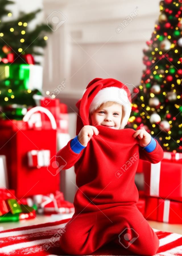 Kind jongen kerstman houden kerstcadeau rode sok. Kerst kous concept. Kind vrolijk gezicht kreeg geschenk in kerst sok. Controleer de inhoud van kerst kous. Vreugde en geluk. Kindertijd momenten