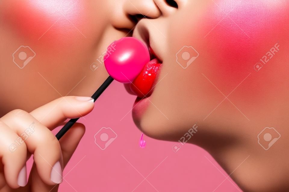 Lizak w ustach, zbliżenie. piękne usta dziewczyny z lolli pop. błyszczące czerwone usta kobiety z językiem. usta lizać ssać chupa chups na różowym tle.