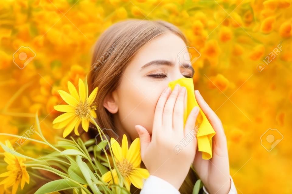 Portrait of an allergic woman surrounded by seasonal flowers wearing bright yellow sweater. Charming girl is blowing her nose near autumn yellow flowers in bloom.