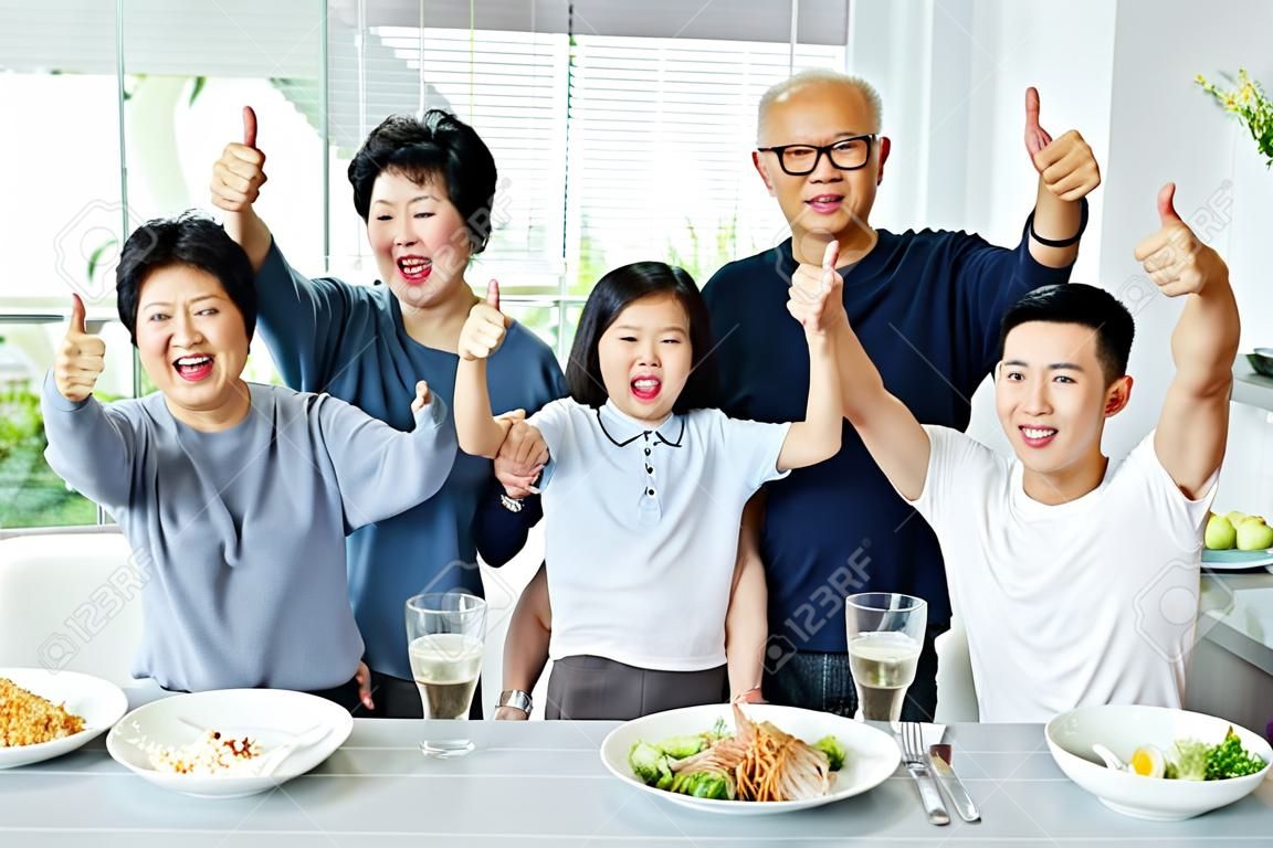 familia asiática de tres generaciones que tienen una comida juntos y mostrando sus pulgares para arriba en casa con felicidad