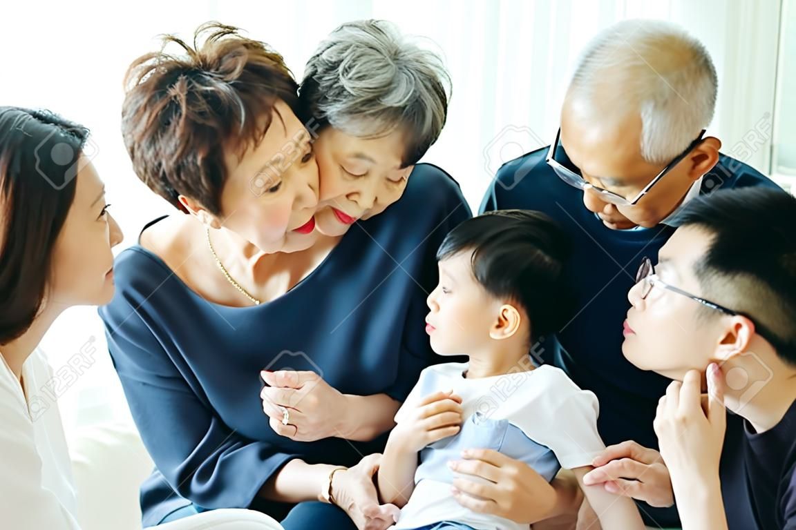 Jongen kussen oma op de wangen met de hele Aziatische familie van drie generaties samen thuis