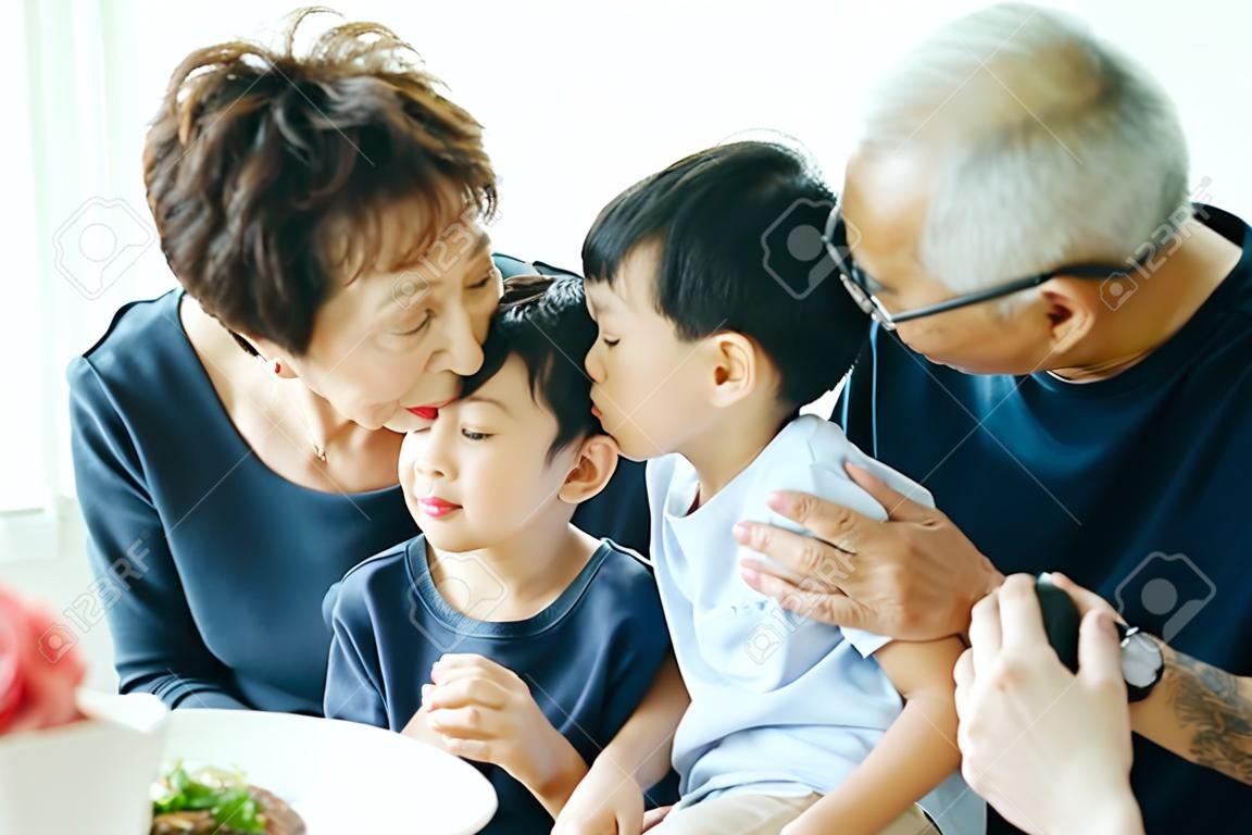 Jongen kussen oma op de wangen met de hele Aziatische familie van drie generaties samen thuis