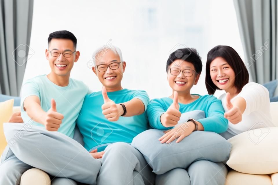 Asian family with adult children and senior parents giving thumbs up and relaxing on a sofa at home together. Happy family time together