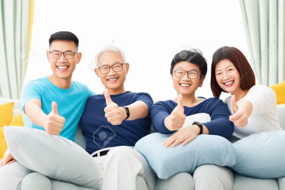 Asian family with adult children and senior parents giving thumbs up and relaxing on a sofa at home together. Happy family time together