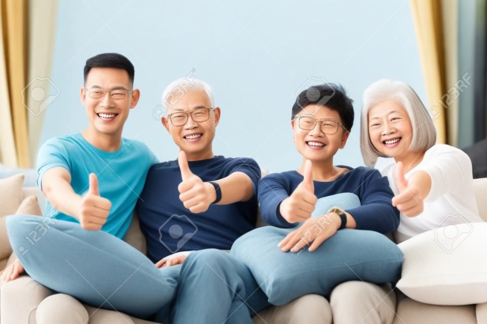 Azjatycka rodzina z dorosłymi dziećmi i starszymi rodzicami podającymi kciuki do góry i relaksującymi się na kanapie w domu. Szczęśliwa rodzina razem