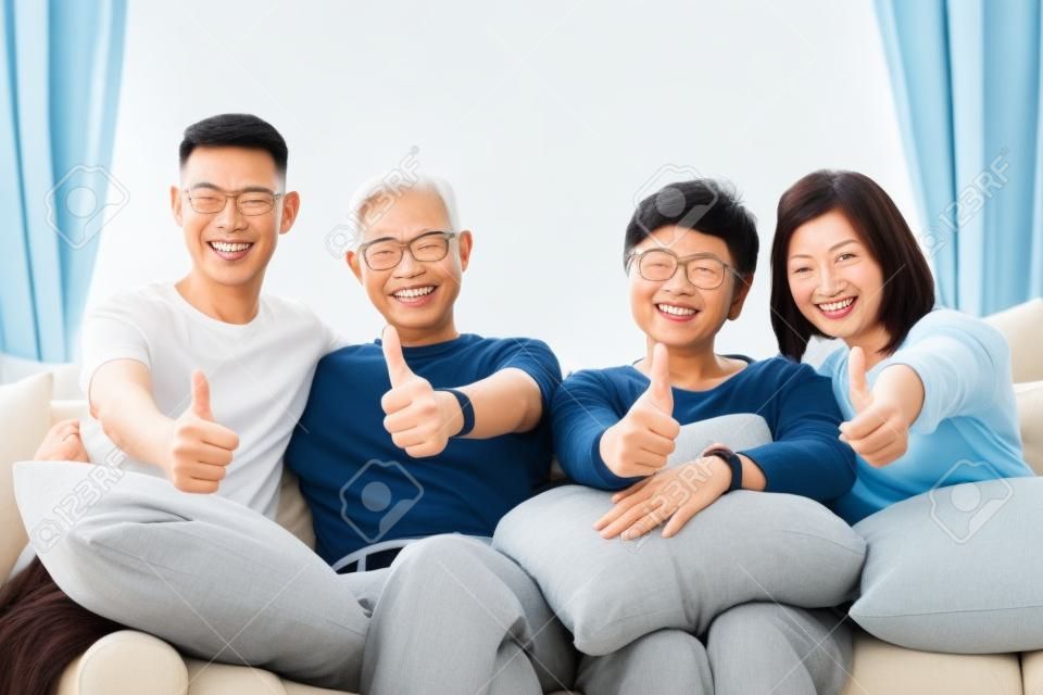 大人の子供と先輩の両親を持つアジアの家族が親指を立て、自宅のソファでリラックスしています。一緒に幸せな家族の時間