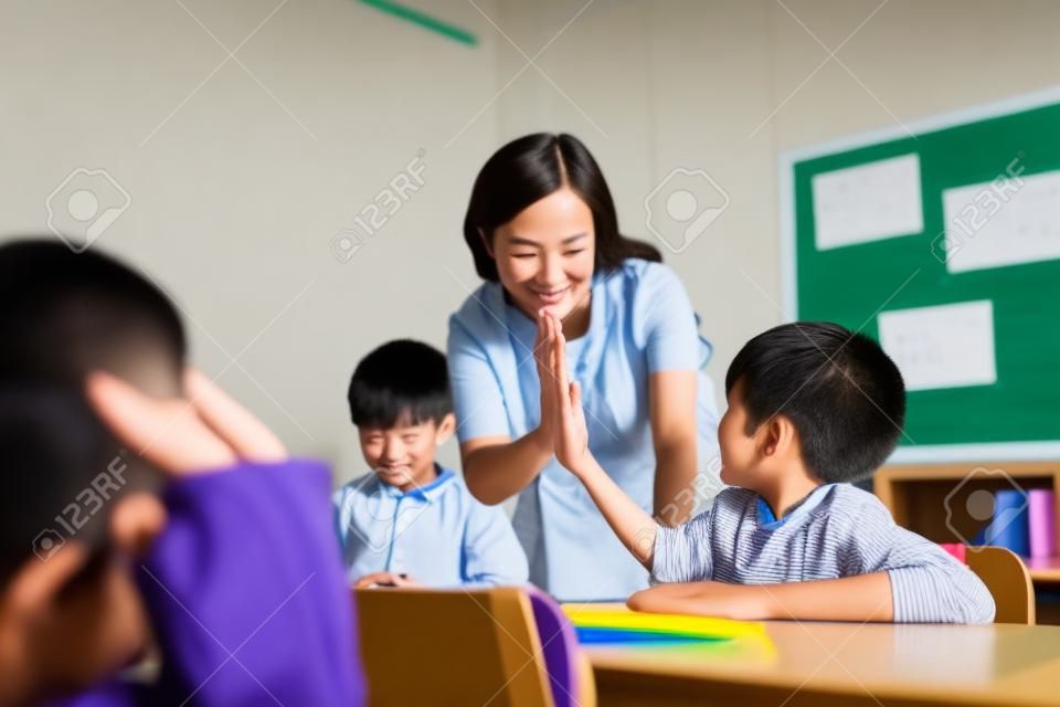 Junger asiatischer Lehrer, der Jungen High Five in der Schule gibt, Erfolg, Leistung, Glück. Asiatischer Schuljunge mit junger Frau in der Klasse.