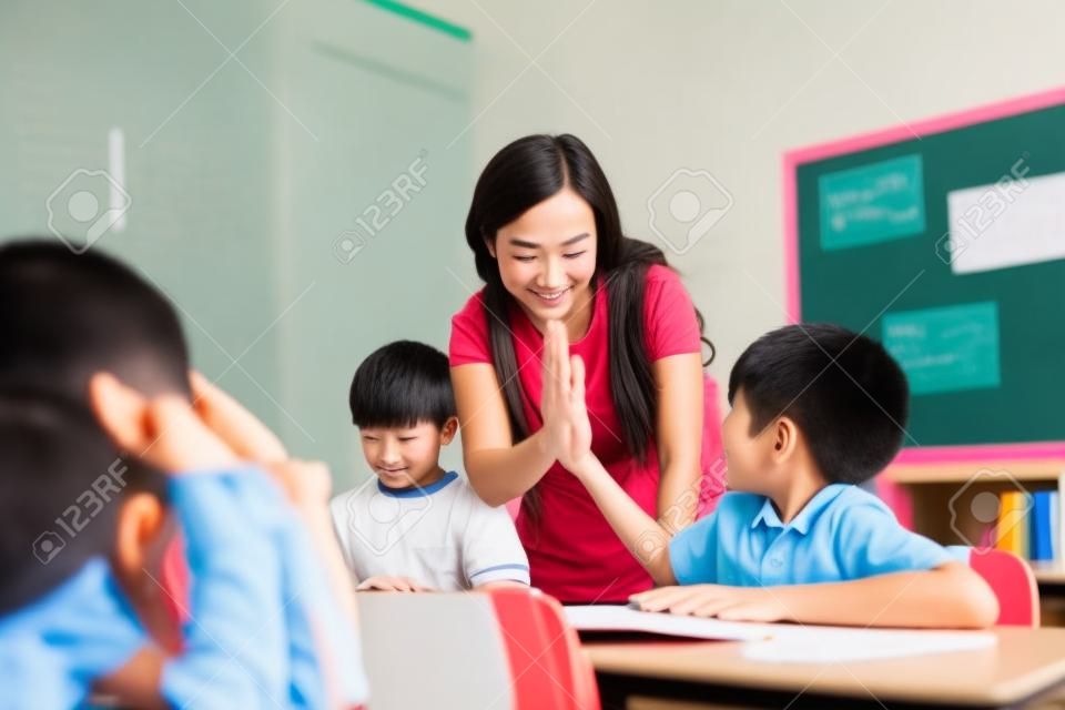 Junger asiatischer Lehrer, der Jungen High Five in der Schule gibt, Erfolg, Leistung, Glück. Asiatischer Schuljunge mit junger Frau in der Klasse.