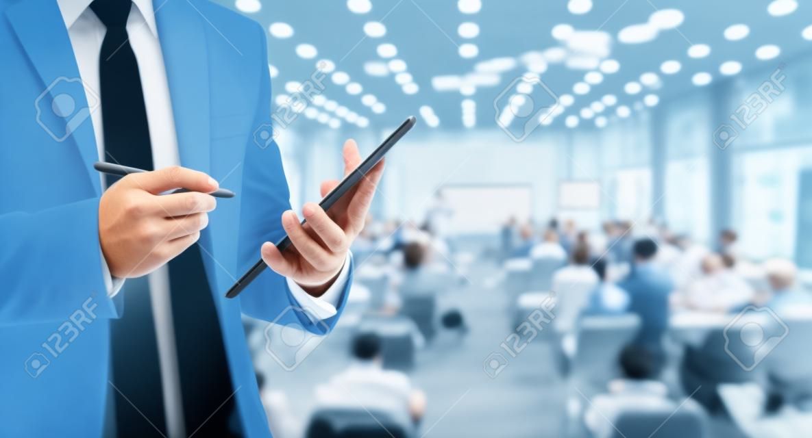 Uomo d'affari con la tavoletta sulla foto sfocata astratta di sala conferenze o sala convegni con partecipanti sfondo