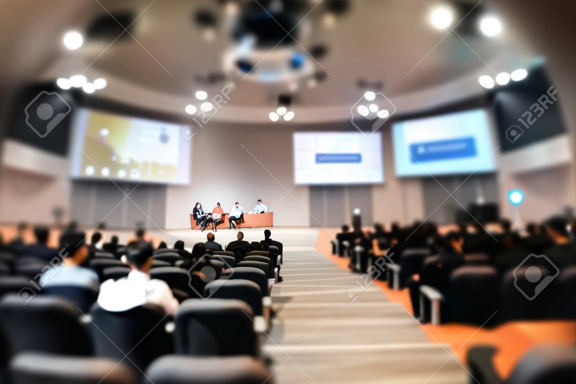 Abstract blurred photo of conference hall or seminar room with speakers on the stage and attendee background