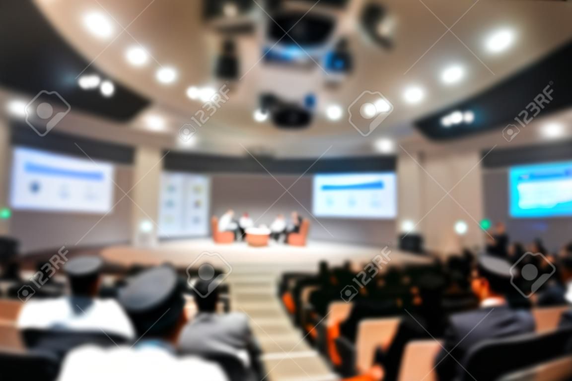 Abstract blurred photo of conference hall or seminar room with speakers on the stage and attendee background