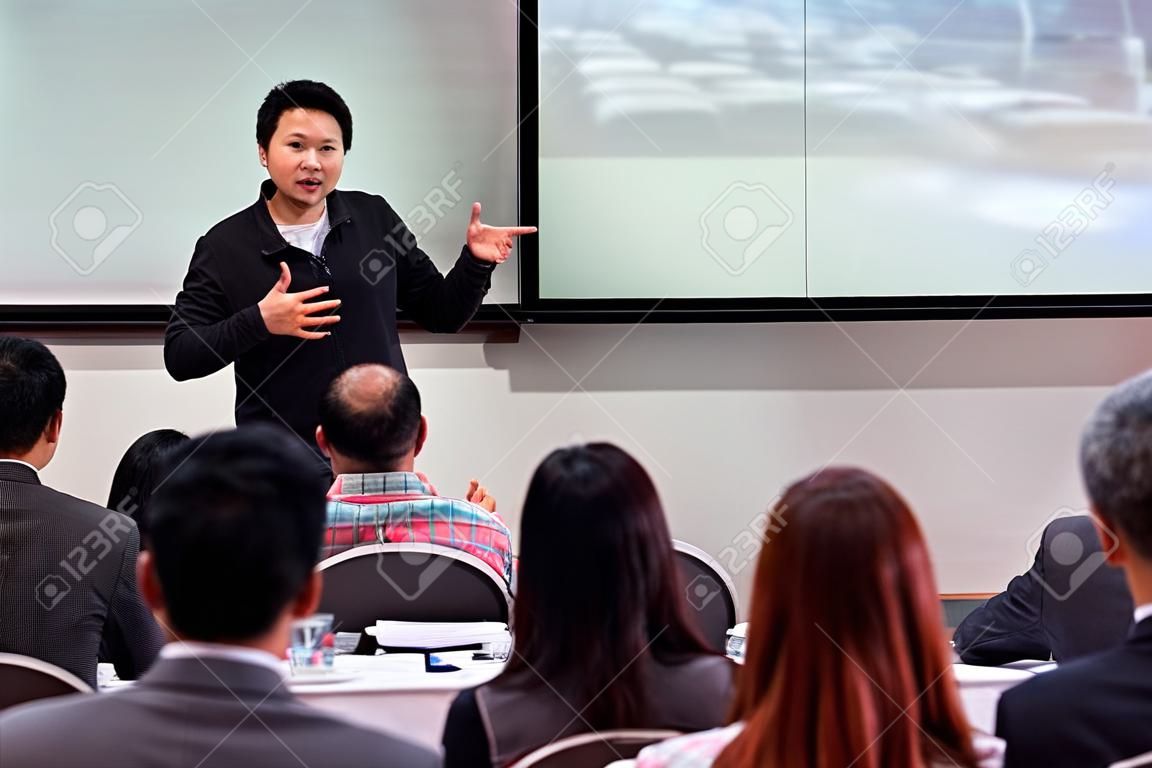 Azjatycki mówca lub wykład w swobodnym garniturze na scenie przed salą prezentujący za pomocą ekranu w sali konferencyjnej lub sali seminaryjnej spotkanie, koncepcja biznesowa i edukacyjna