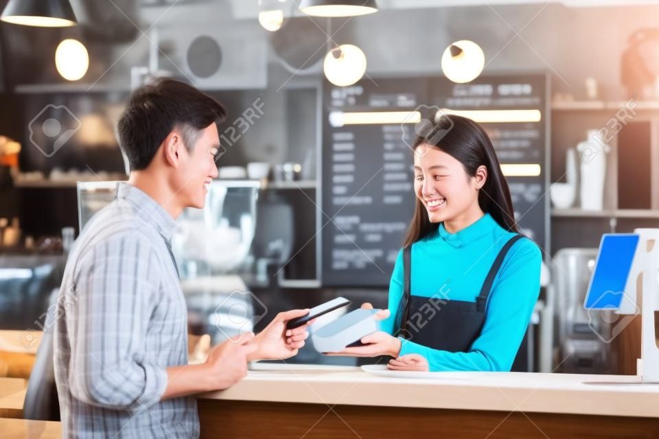 Asian customer man paying via contactless channel by mobile banking application to Asian Small business owner at the table in coffee shop, Small business owner and startup in coffee shop concept