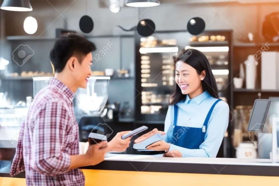 Asian customer man paying via contactless channel by mobile banking application to Asian Small business owner at the table in coffee shop, Small business owner and startup in coffee shop concept