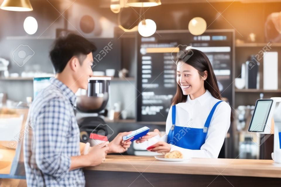 Azjatycki klient klient płaci kanałem zbliżeniowym przez aplikację bankowości mobilnej właścicielowi azjatyckiej małej firmy przy stole w kawiarni, właściciel małej firmy i startup w koncepcji kawiarni