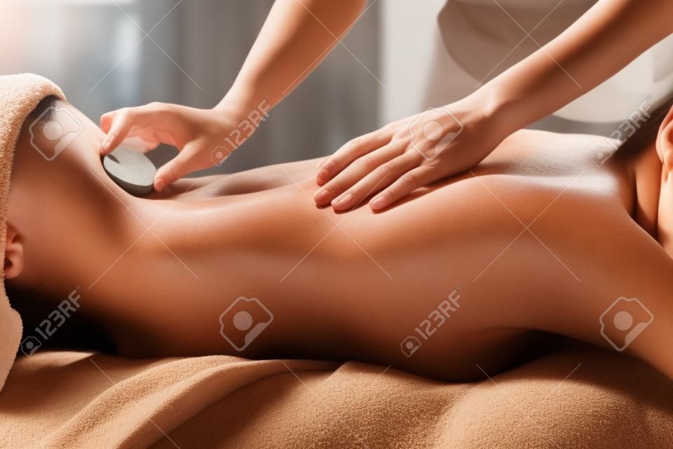 Frau, die heiße Steinmassage im Badekurortsalon erhält. Beauty-Behandlungskonzept