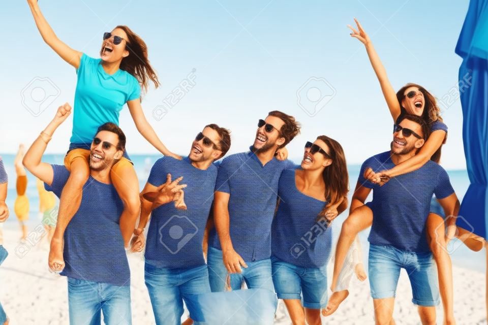 Gruppe von Freunden, die am Strand spazieren gehen, Spaß haben, Frau huckepack auf Mann, lustiger Urlaub