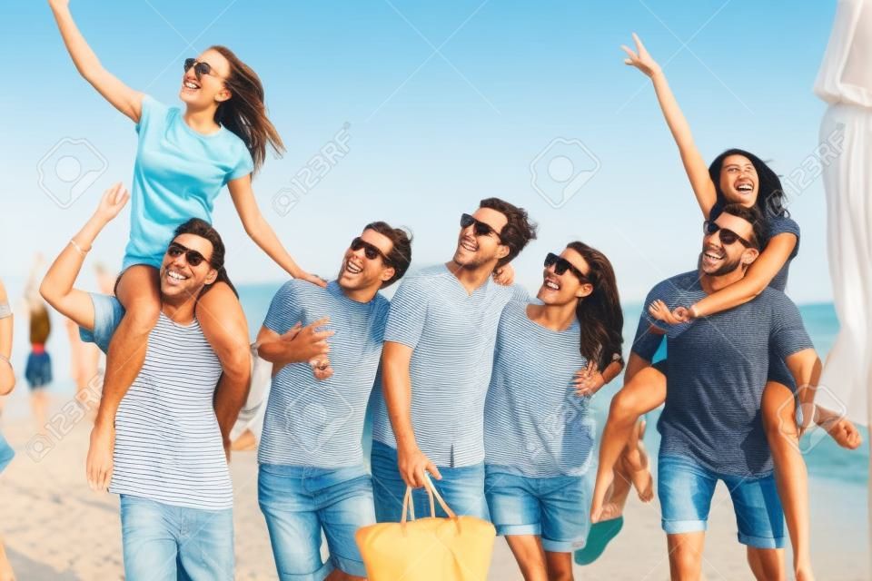 Gruppe von Freunden, die am Strand spazieren gehen, Spaß haben, Frau huckepack auf Mann, lustiger Urlaub