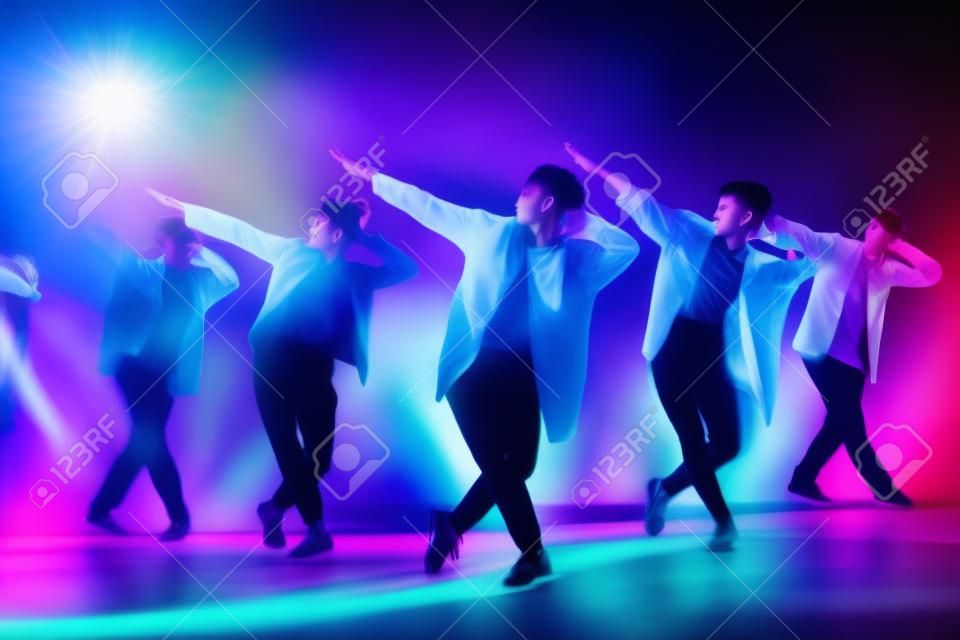 Młody nowoczesny taniec grupa sześciu dorosłych młodych ludzi ćwiczy taniec na kolorowym tle. modnie ubrani młodzieńcy poruszający się nad niewyraźnymi kolorowymi światłami klubu disco
