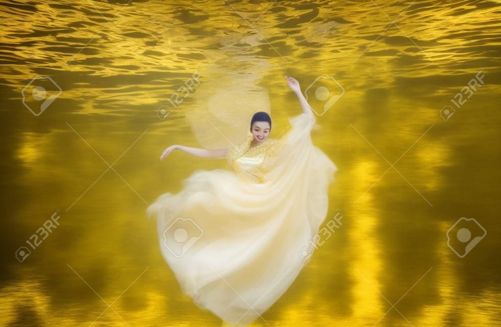 beautiful young woman in gold dress, evening dress floating weightlessly elegantly floating in the water in the pool