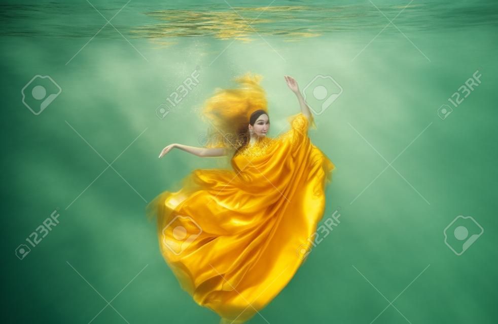 Schöne junge frau in goldenem kleid, abendkleid schwebend schwerelos elegant schwebend im wasser im pool