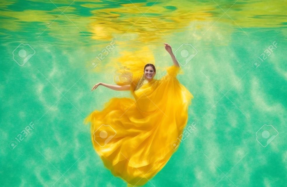 beautiful young woman in gold dress, evening dress floating weightlessly elegantly floating in the water in the pool
