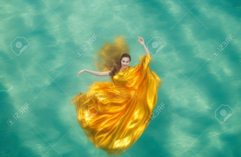 Schöne junge frau in goldenem kleid, abendkleid schwebend schwerelos elegant schwebend im wasser im pool