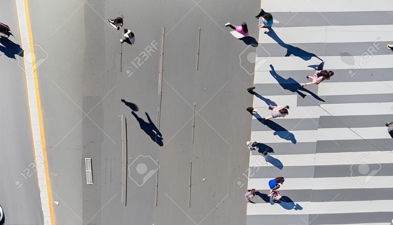 Vista aérea superior del grupo de personas que caminan en la ciudad de la calle con un paso de peatones en la carretera de tráfico de transporte con la luz del sol y la silueta de la sombra
