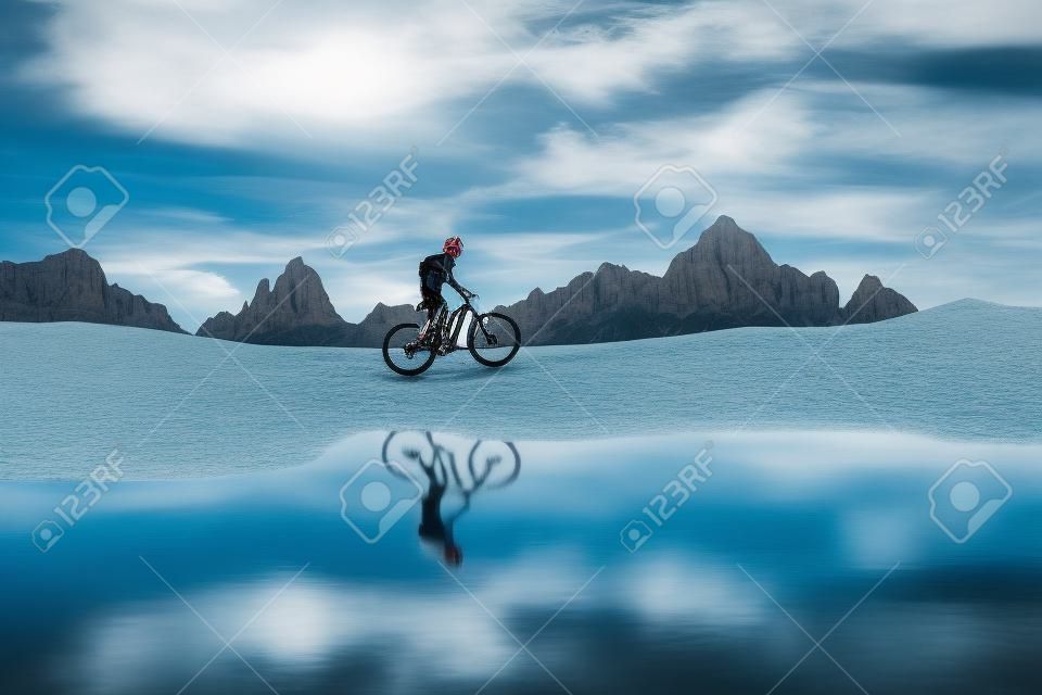 mooie vrouw rijden haar elektrische mountainbike de Three Peaks Dolomites, reflecteren zichzelf in het blauwe water van een koud bergmeer