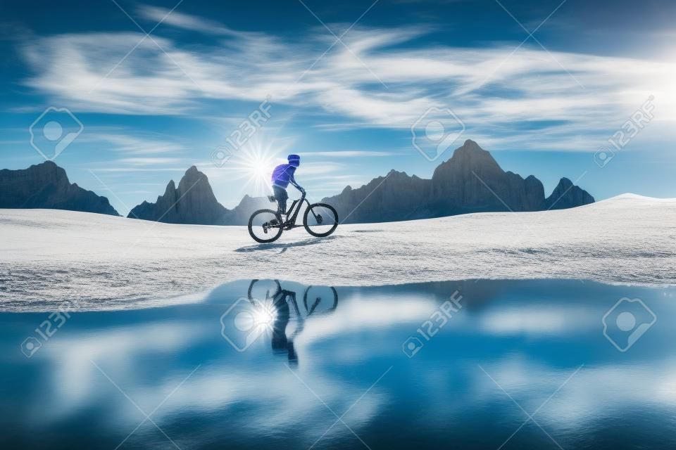 nette Frau, die mit ihrem elektrischen Mountainbike die Drei Zinnen Dolomiten fährt und sich im blauen Wasser eines kalten Bergsees widerspiegelt