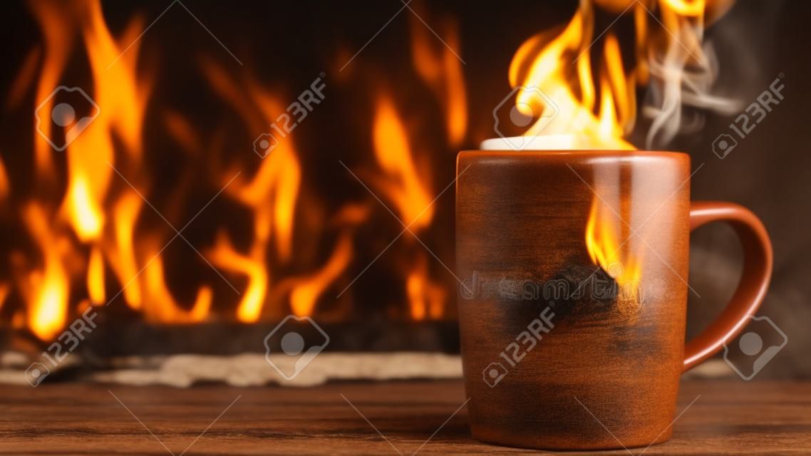 Steaming cup of hot beverage coffee or tea on wooden board by burning fireplace. Steam rising from cup. copyspace. close up.